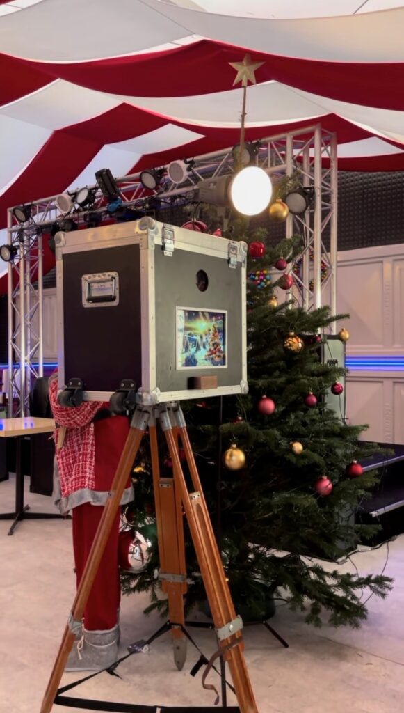 Fotoautomat neben geschmücktem Weihnachtsbaum bei einer Weihnachtsfeier